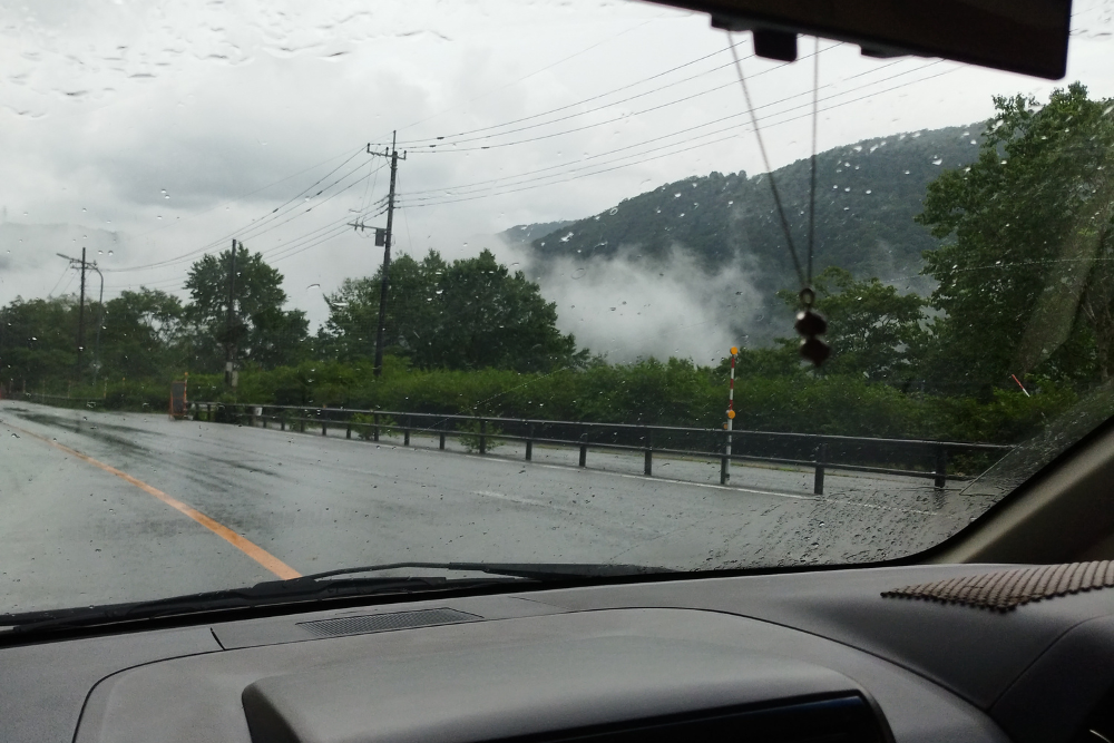 「雨の車窓から見える山と道路」